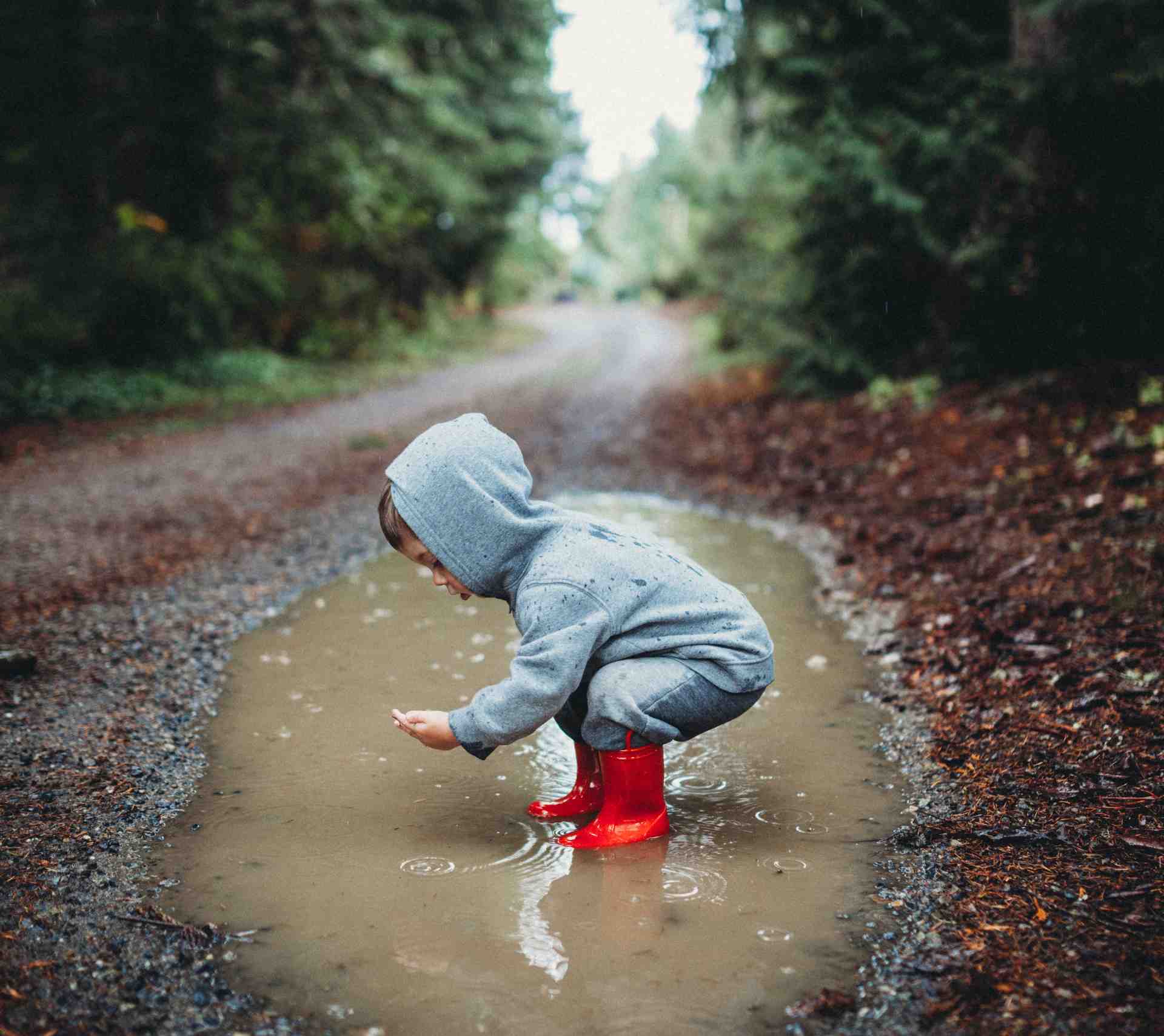 Kind in roten Gummistiefeln spielt neugierig in einer Pfütze – symbolisiert Freude und Entdeckergeist im Familienalltag -familienfreundliche Produkte